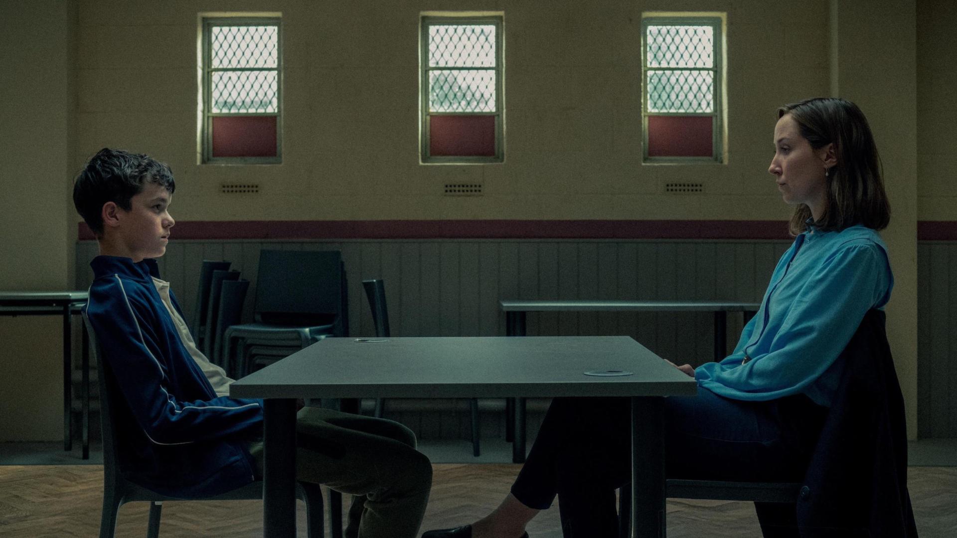 Young white boy and older white woman sit opposite each other in a young protections unit